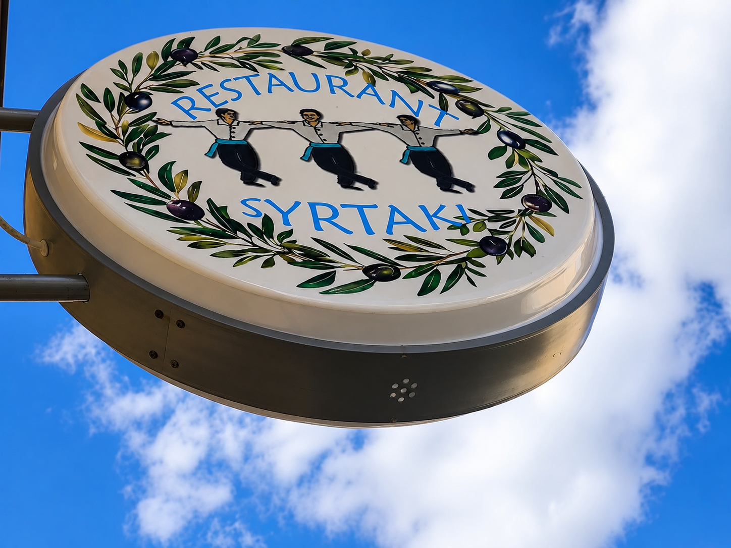 Schild des Restaurant Syrtaki mit Sirtaki-Tänzern und Olivenzweigen