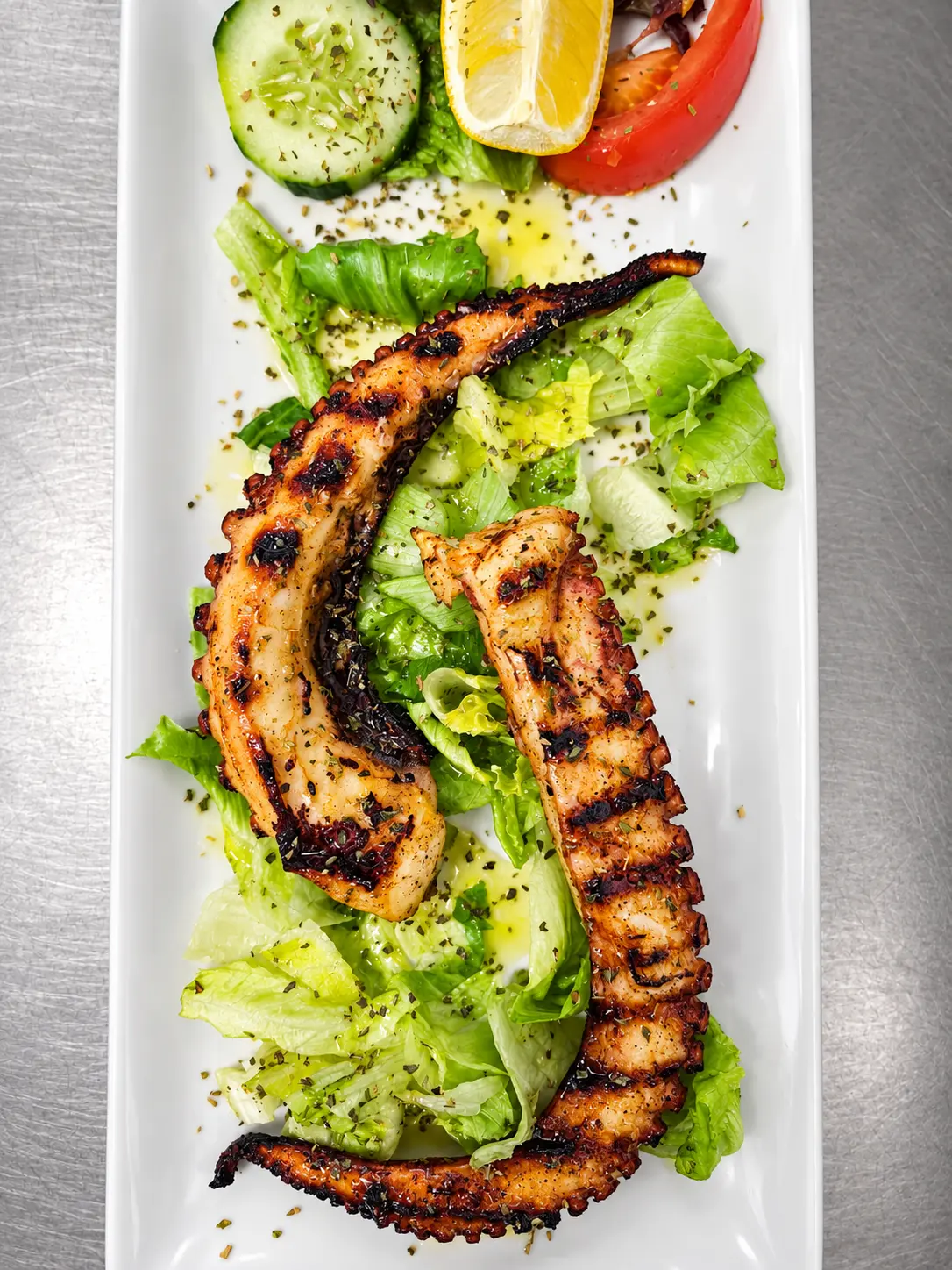 Oktopus vom Grill auf Salat mit Gurke, Tomate und Zitrone.